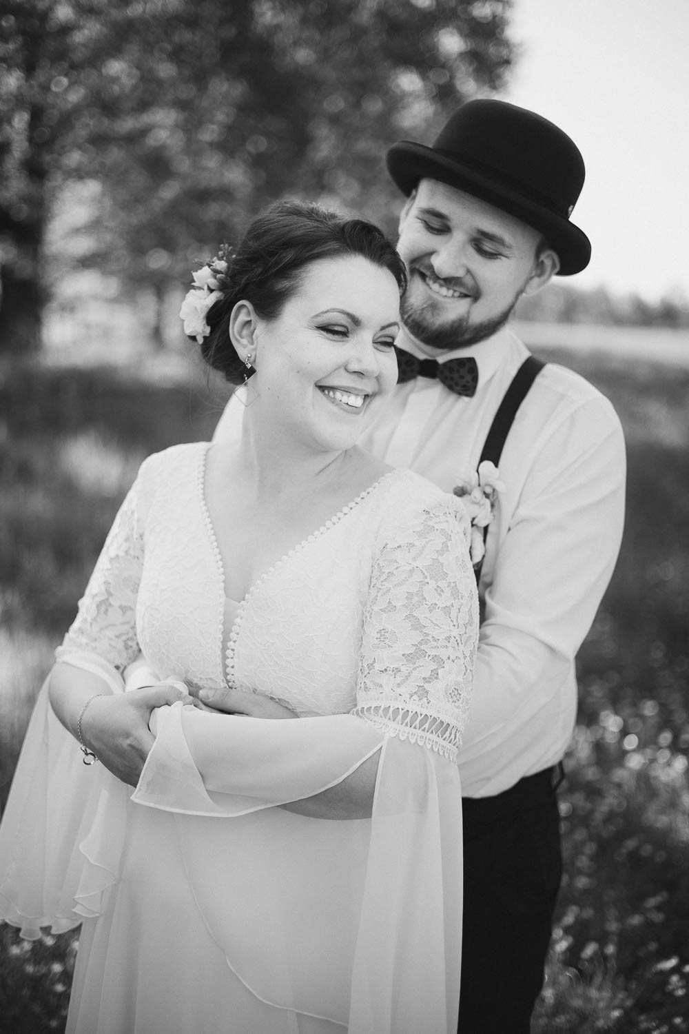 Černobílá fotka novomanželů během prvního novomanželského focení v den svatby. Ženich stojí za nevěstou a drží ji kolem pasu.